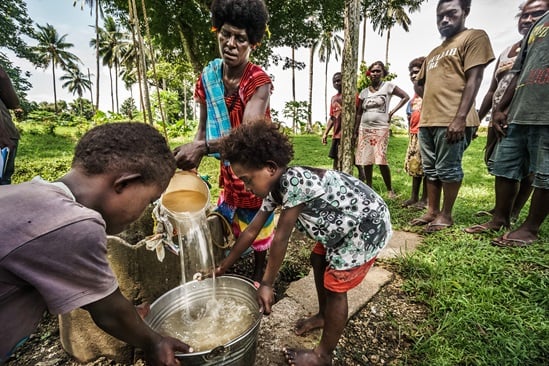 Kids holding a bucket while woman pours water into the bucket